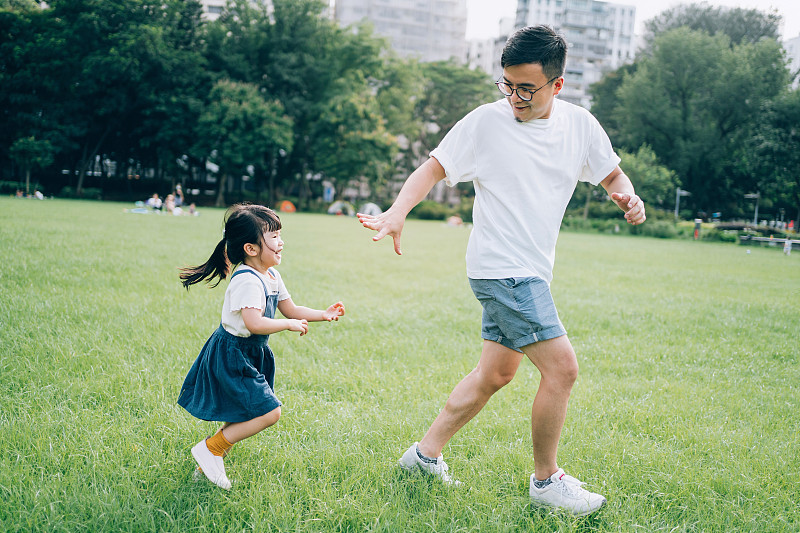 快乐的亚洲小女孩和年轻的亚洲父亲在户外玩，在草坪上奔跑，享受自然和夏季在城市公园。亲情的生活方式。无忧无虑、自由的概念图片下载