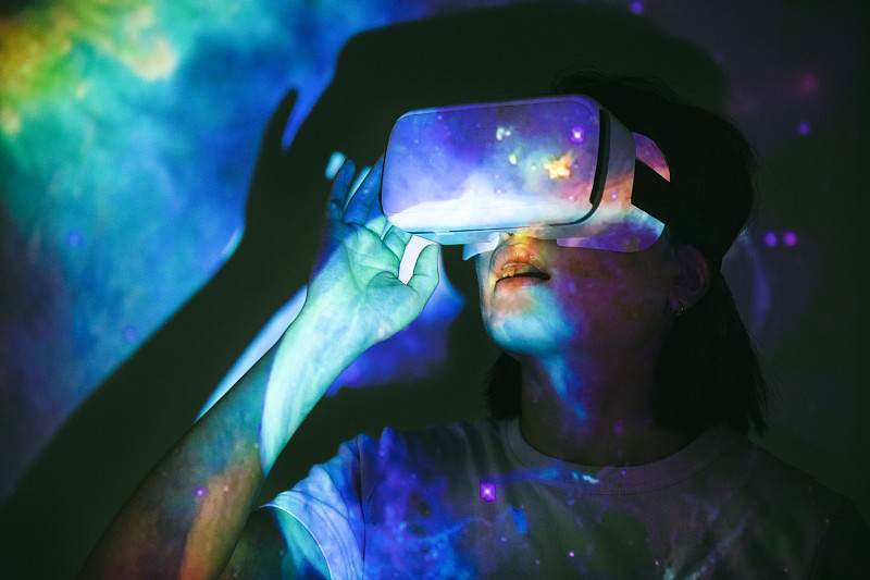 一名亚洲女子戴着虚拟现实头戴式耳机，头上投影着外太空的影像图片下载