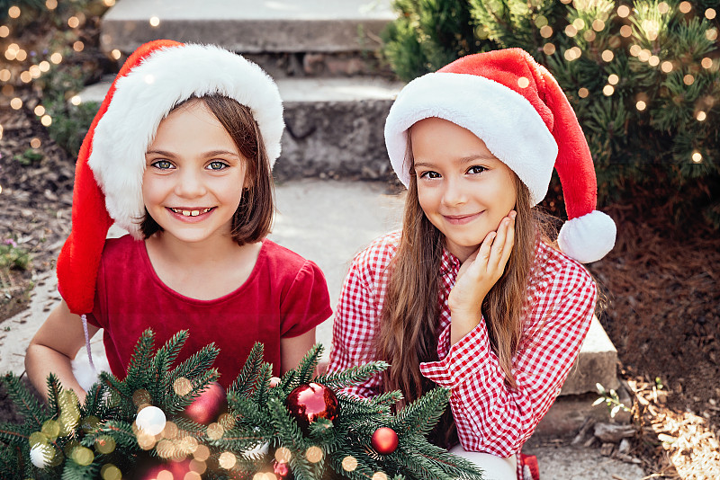 圣诞快乐。画像中的两个快乐有趣的儿童女孩戴着圣诞帽，戴着圣诞花环图片下载