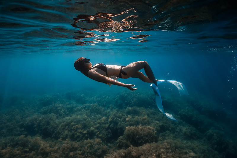 带鳍的自由潜水妇女在热带海洋的水下和水面滑翔。图片下载