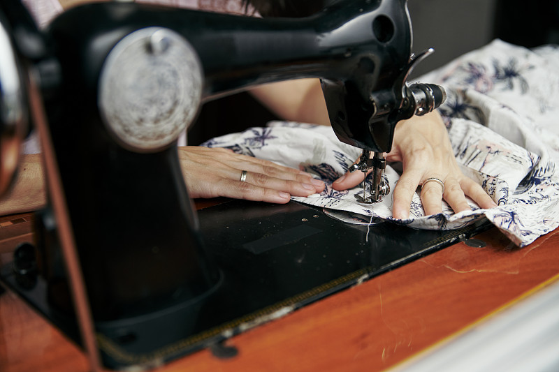 特写:年轻的黑发女子在家里的旧缝纫机上缝纫。自主创业，在家工作。侧视图摄影图片