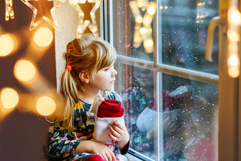 学龄前的小女孩拿着杯子圣诞老人靴子的礼物叫Nikolausstiefel在德语。快乐的孩子在冬天，在挂着圣诞彩灯的窗边等待节日。舒适的家庭庆祝圣诞节。图片下载