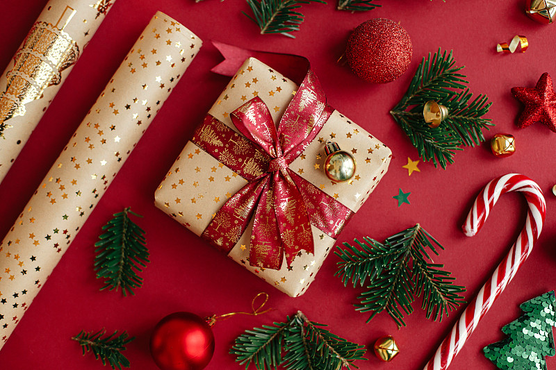 圣诞快乐，节日快乐!现代圣诞平躺。时尚的圣诞礼物，包装纸，杉木树枝，糖果拐杖和小玩意组成的红色背景。节日的旗帜图片下载