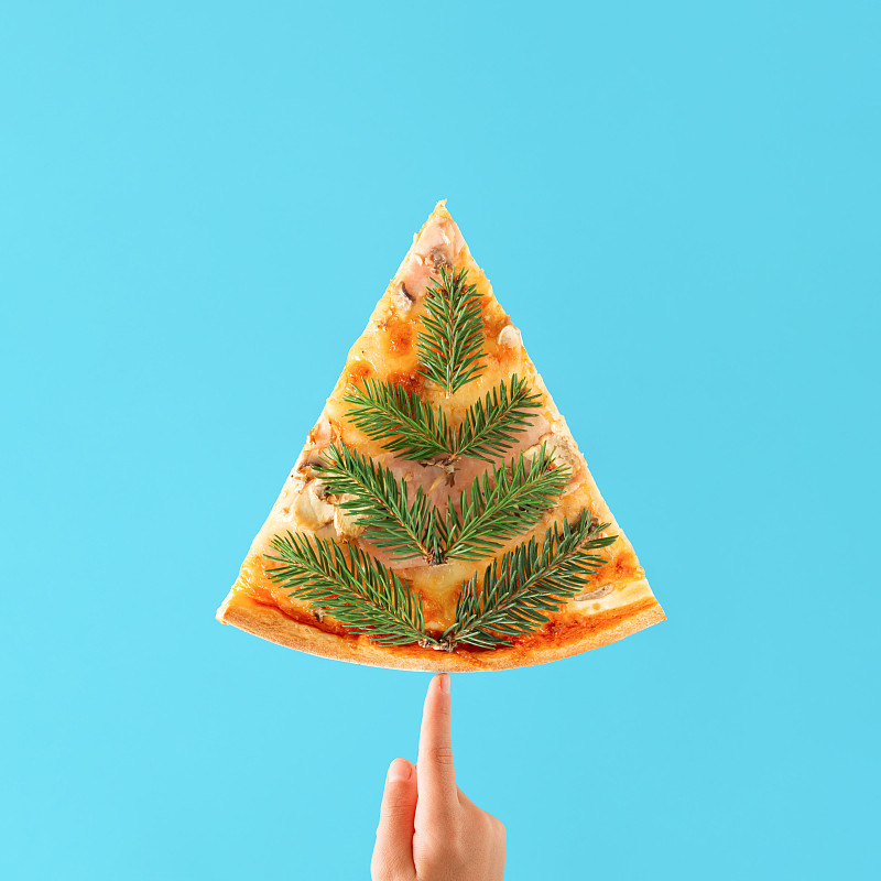 创意圣诞树与孩子的手和三角形披萨覆盖冷杉树枝。最小抽象圣诞卡与孤立的生动的蓝色背景。新年美食派对的概念。图片下载