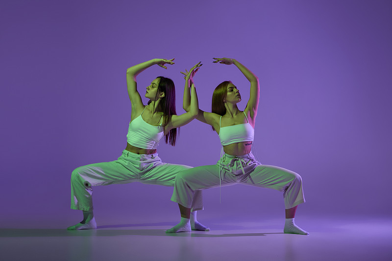 实验舞蹈。两个年轻女孩在运动，动作孤立在紫色背景上。情感，爱情，风格，青春，音乐和时尚图片下载