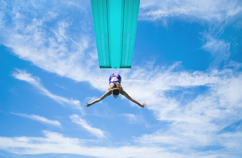 少女(16-17岁)从跳水板上跳下来，低角度观看，对着天空图片下载