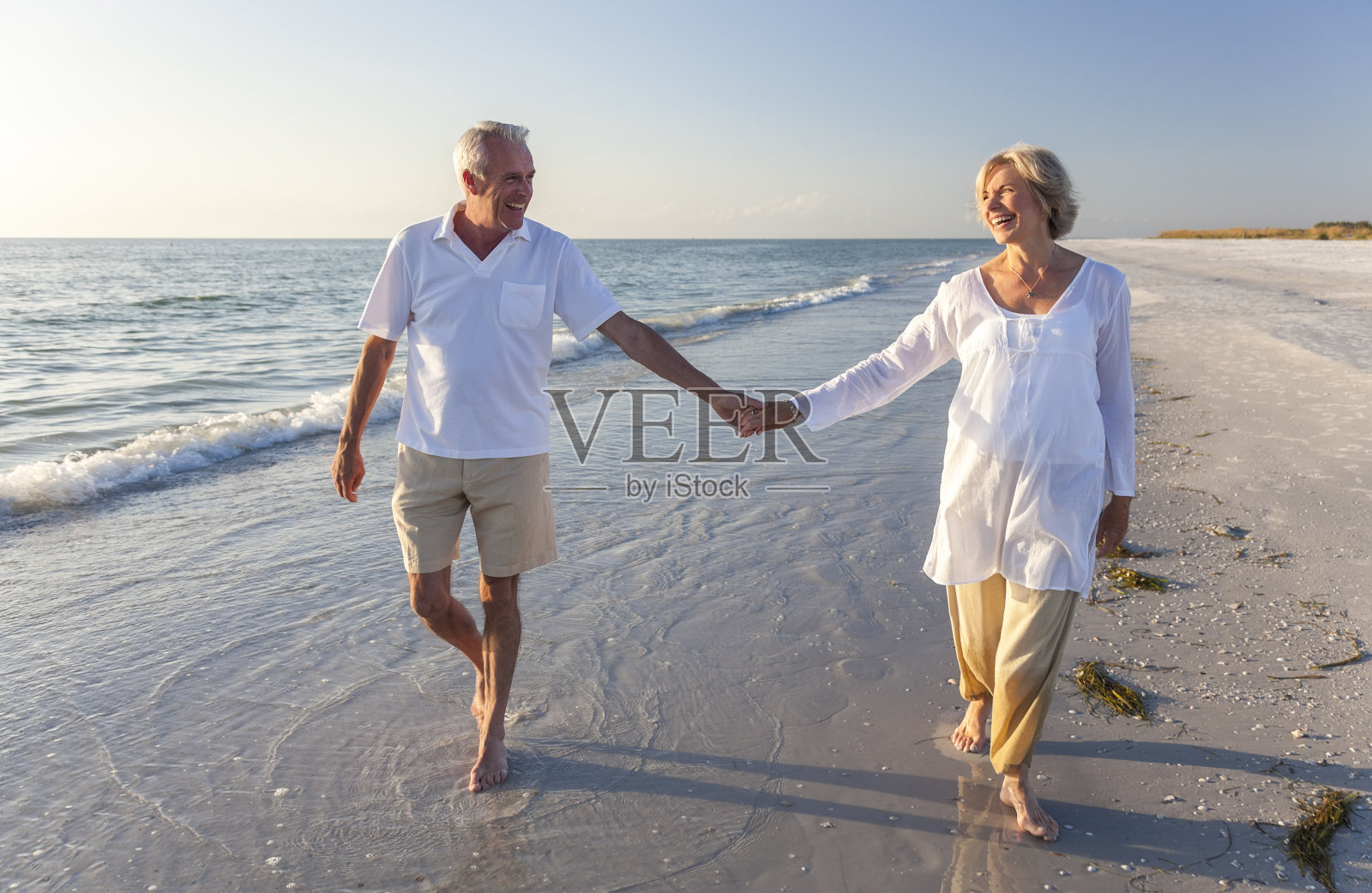 微笑的老年夫妇在海滩上牵着手照片摄影图片