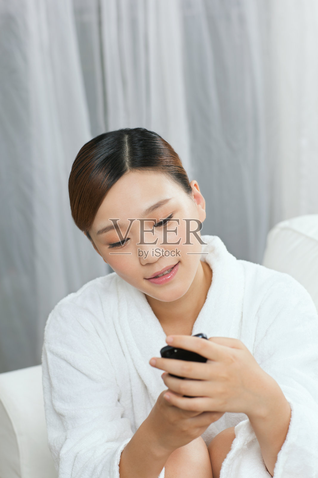 年轻女子穿着浴袍坐在沙发上发短信照片摄影图片