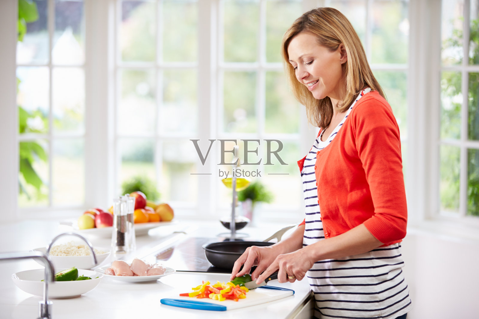 穿着开襟羊毛衫的女人在白色的厨房里切菜照片摄影图片