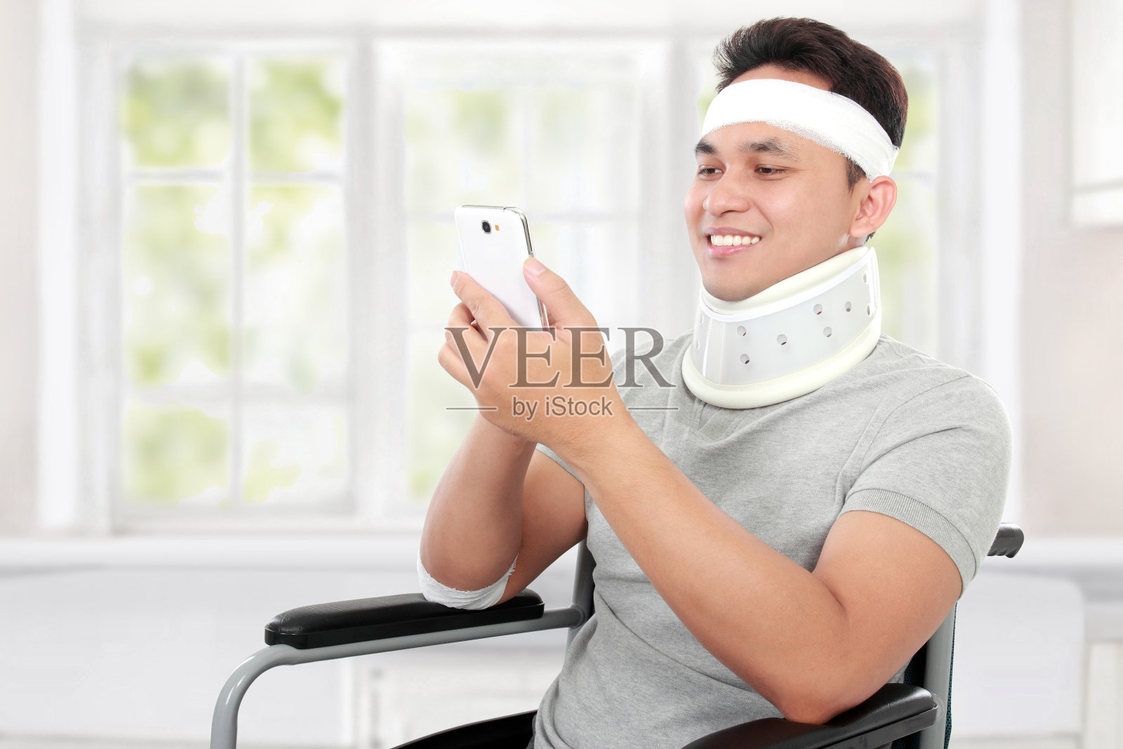 受伤的年轻人坐在轮椅上玩他的智能手机照片摄影图片