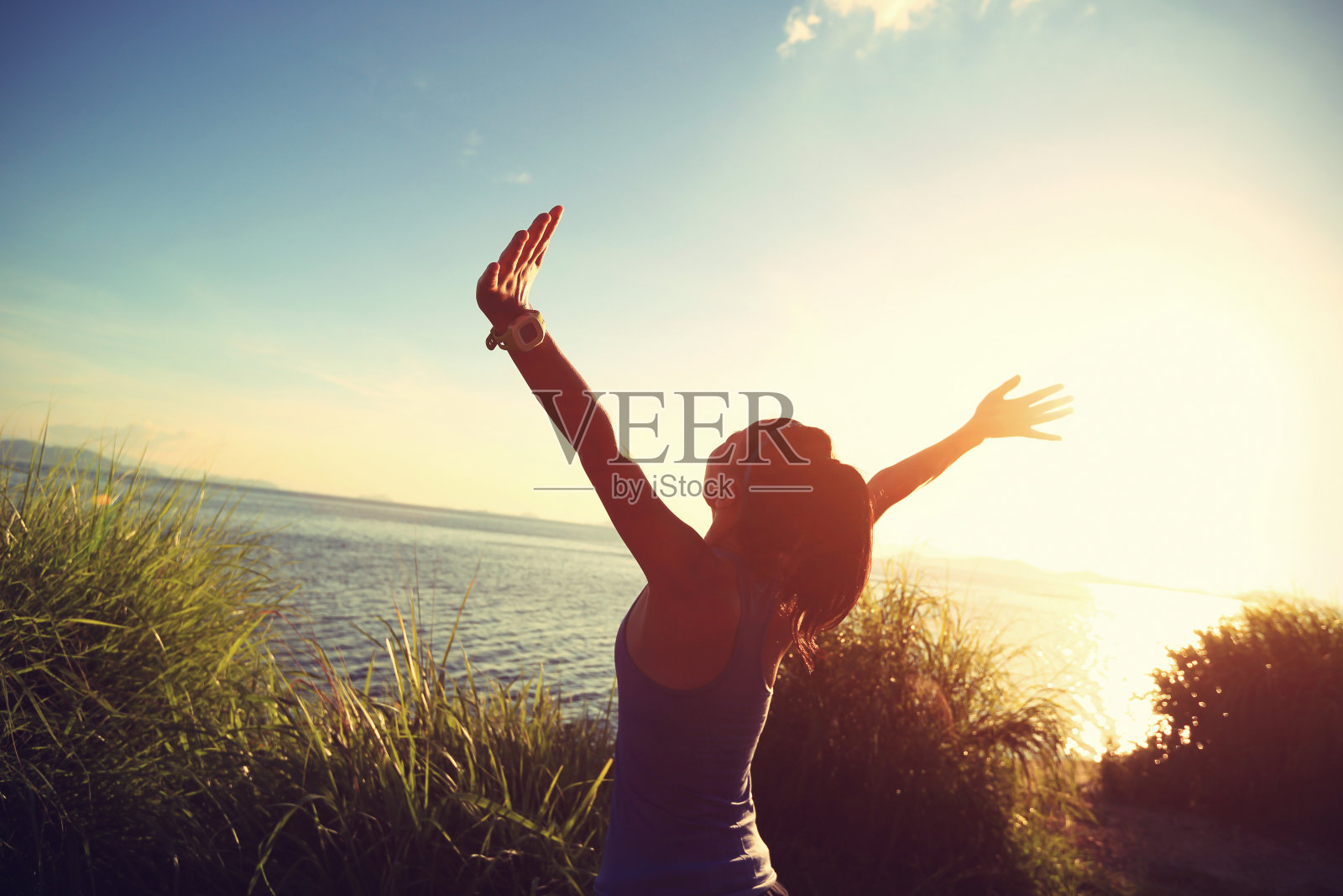 欢呼的年轻女子跑步者在日出的海边张开双臂照片摄影图片