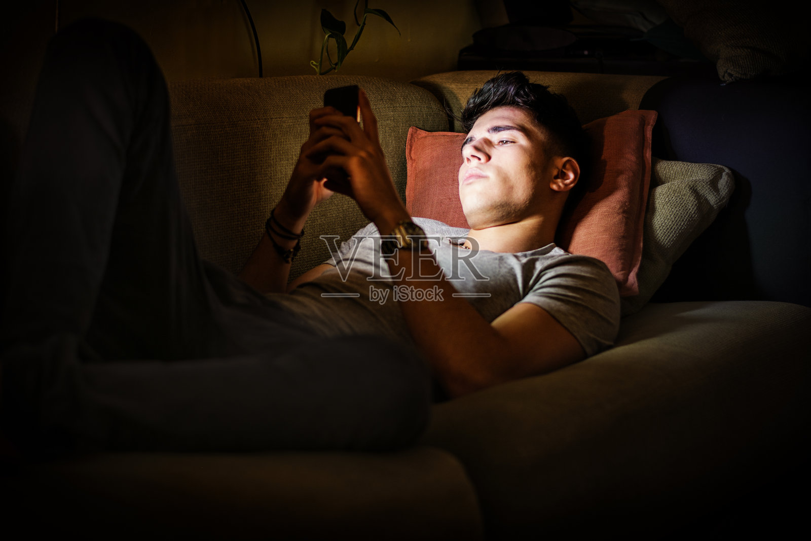 被手机灯光照亮的沙发上的年轻人照片摄影图片