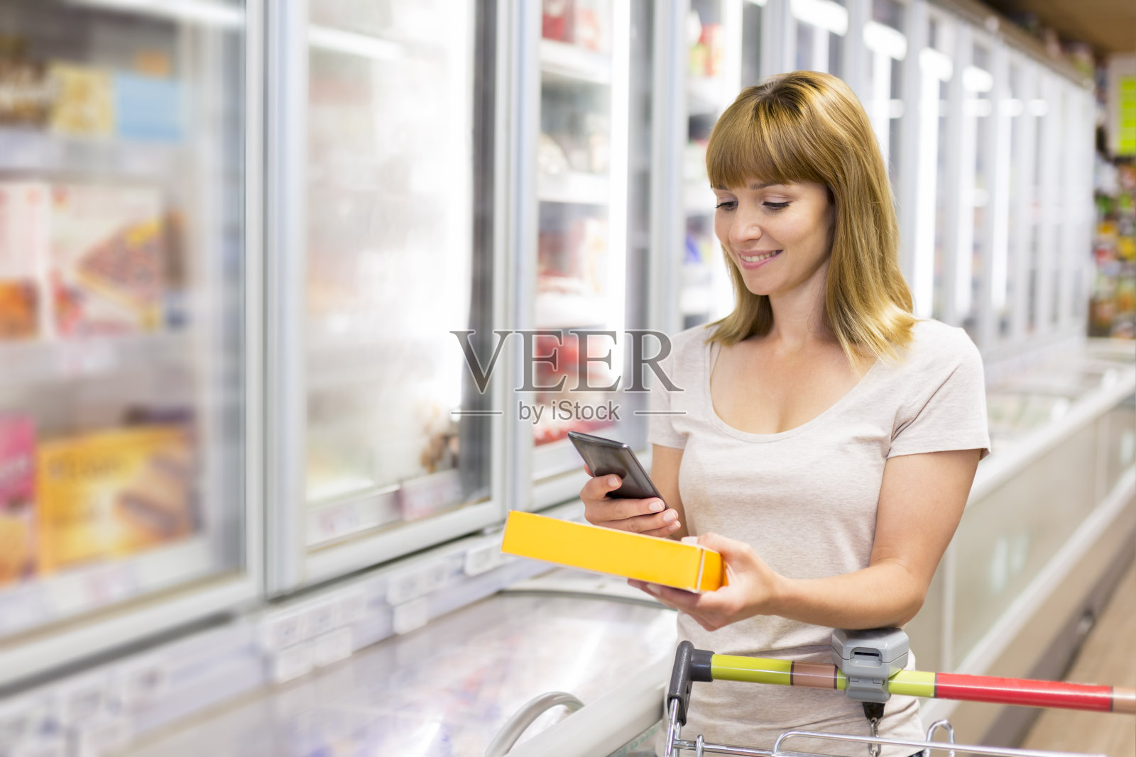 快乐的年轻女子在超市用手机发短信。照片摄影图片