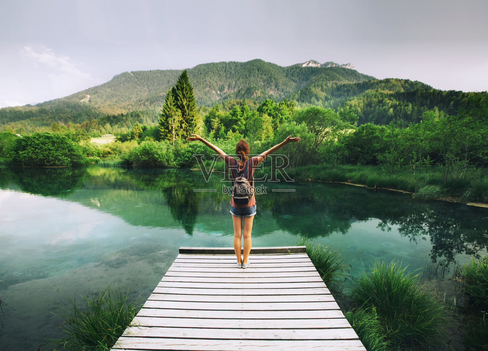 一名年轻女子站在木桥上，双手高举，背景是大自然。照片摄影图片