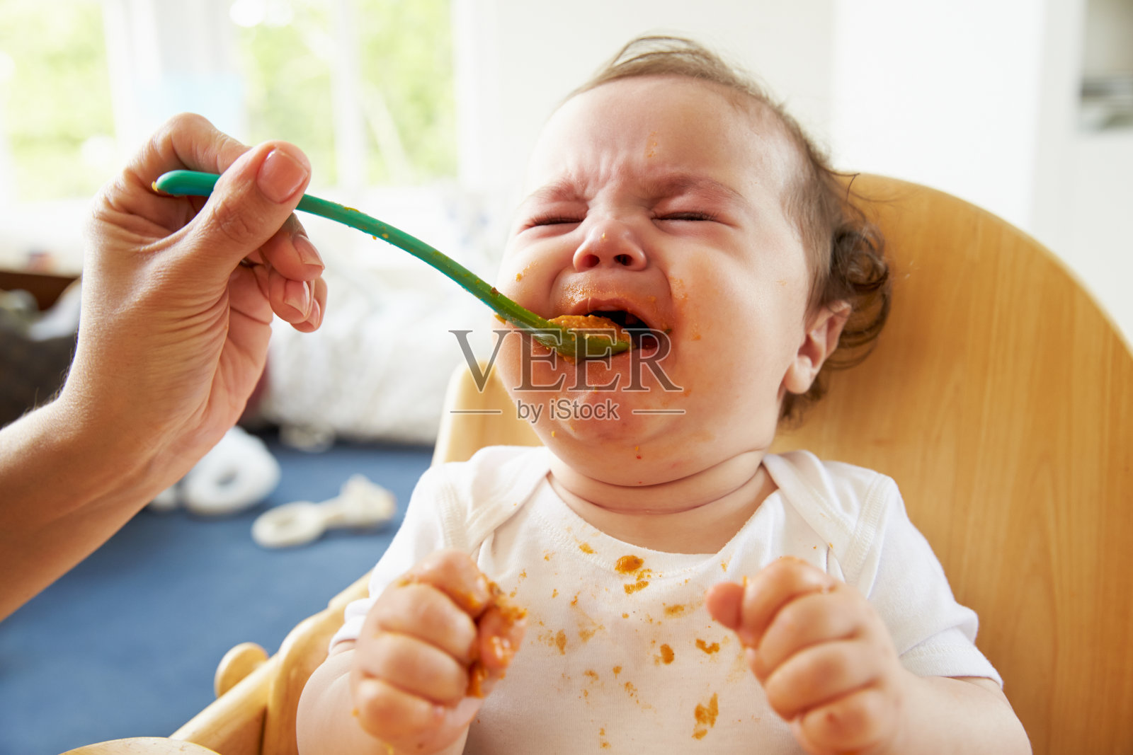 不快乐的婴儿被喂养在高椅子在用餐时间照片摄影图片