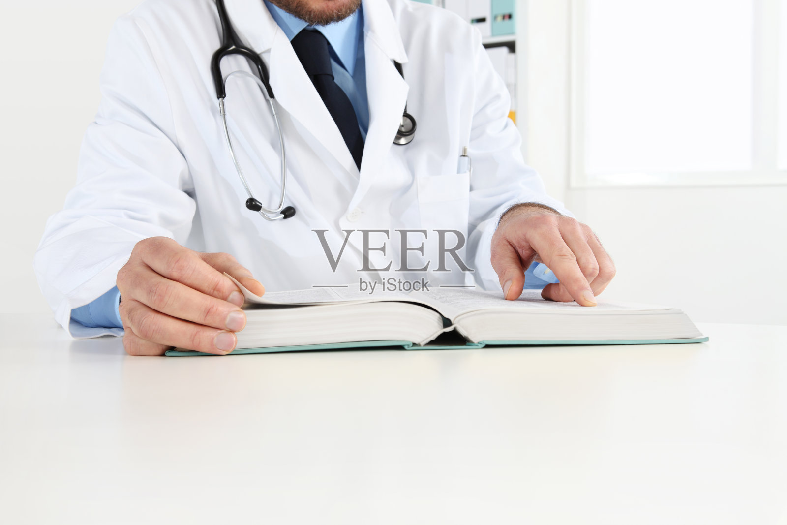 医生在办公桌面阅读一本医学书籍。保健、医疗和制药概念。照片摄影图片