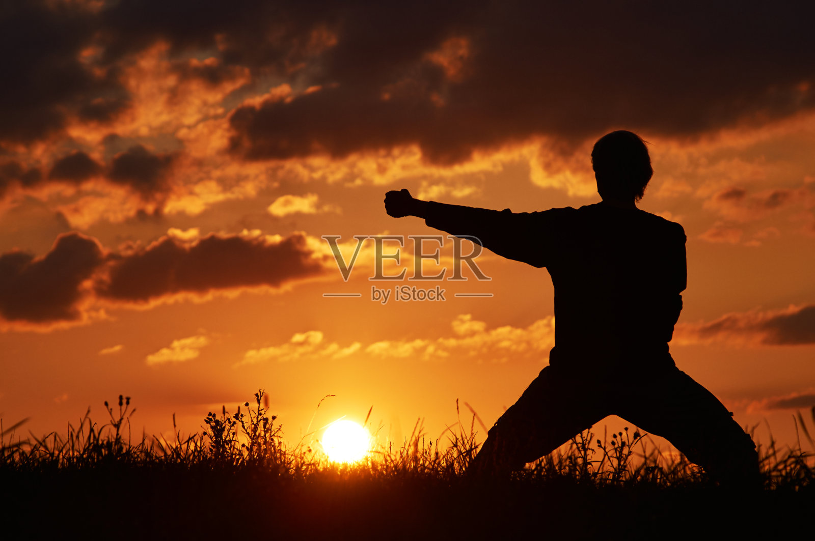 日落时分，一名男子在草地上练习空手道。照片摄影图片