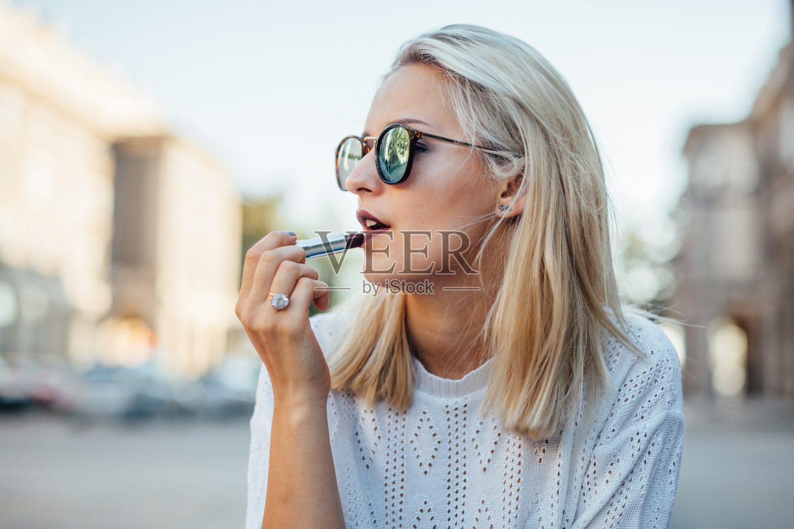 年轻时尚的女人正坐着画嘴唇。城市回来照片摄影图片