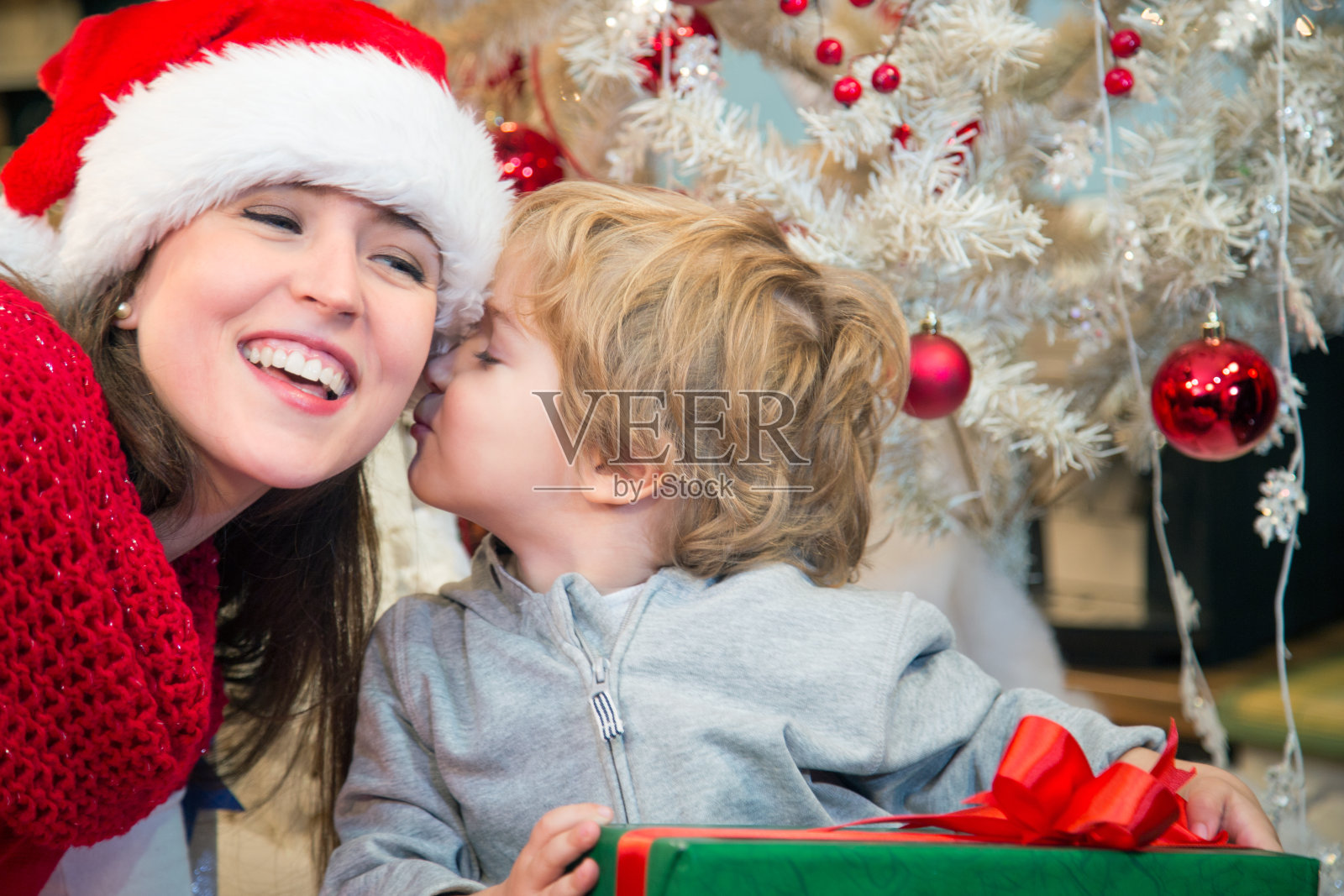 儿子在圣诞节的早晨亲吻他的母亲。照片摄影图片