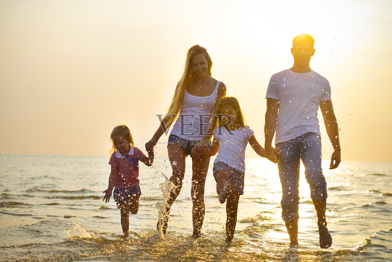 幸福的年轻的家庭在日落时在海滩上跑步。照片摄影图片