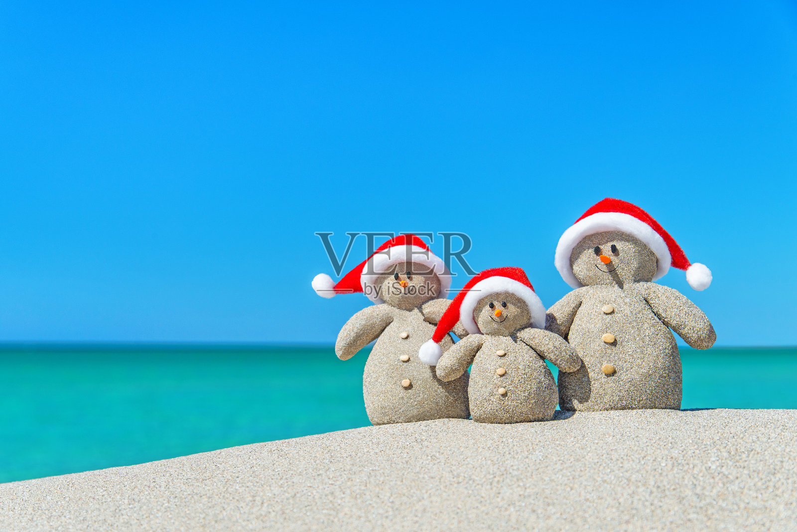 戴着圣诞帽的圣诞雪人一家在热带海滩。照片摄影图片