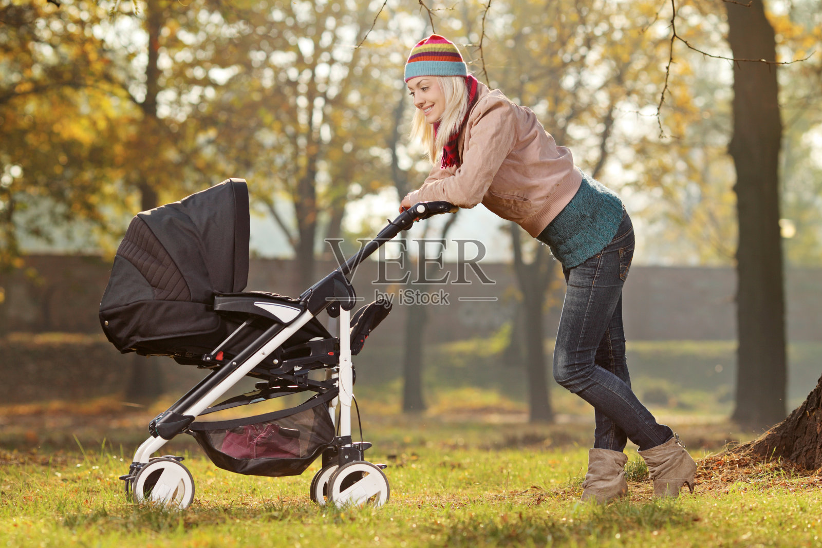 年轻的妈妈推着婴儿车在公园里散步照片摄影图片