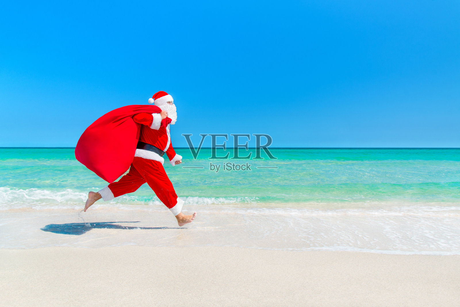 圣诞老人带着装满礼物的袋子在海滩上奔跑照片摄影图片