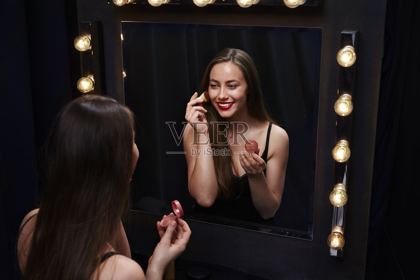 漂亮的年轻女子在镜子里用腮红照片摄影图片