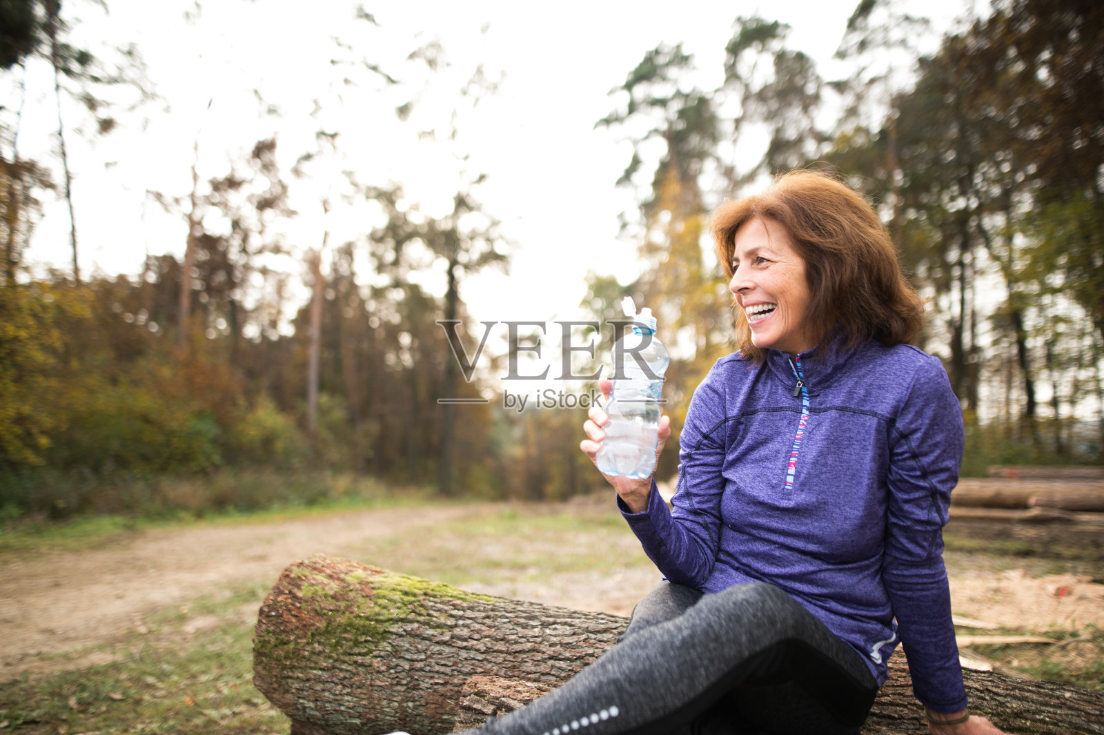 资深跑步者坐在木头上休息，喝水。照片摄影图片