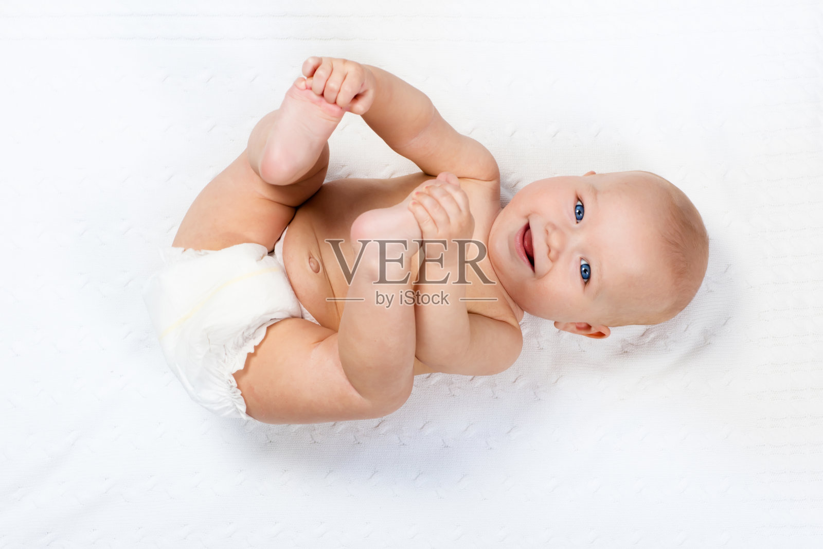 小婴儿穿着尿布在白色的针织毯子上玩耍照片摄影图片
