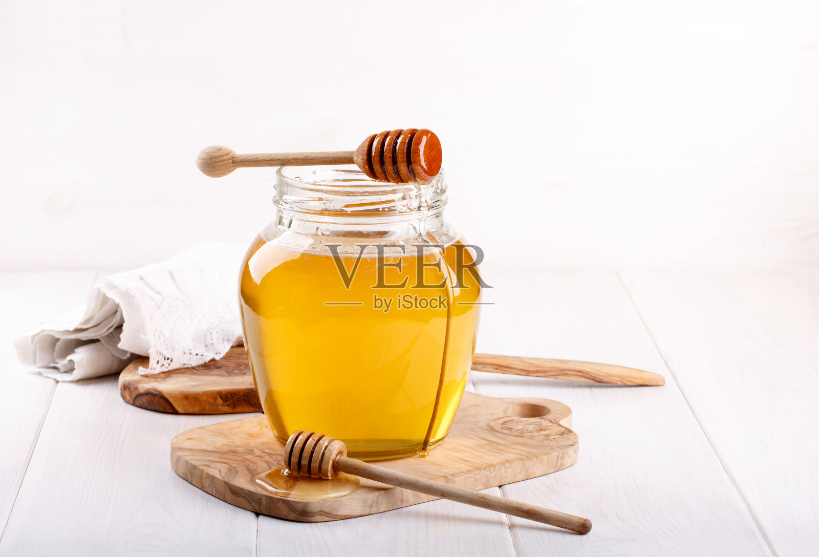 蜂蜜的玻璃罐和白色的木勺照片摄影图片