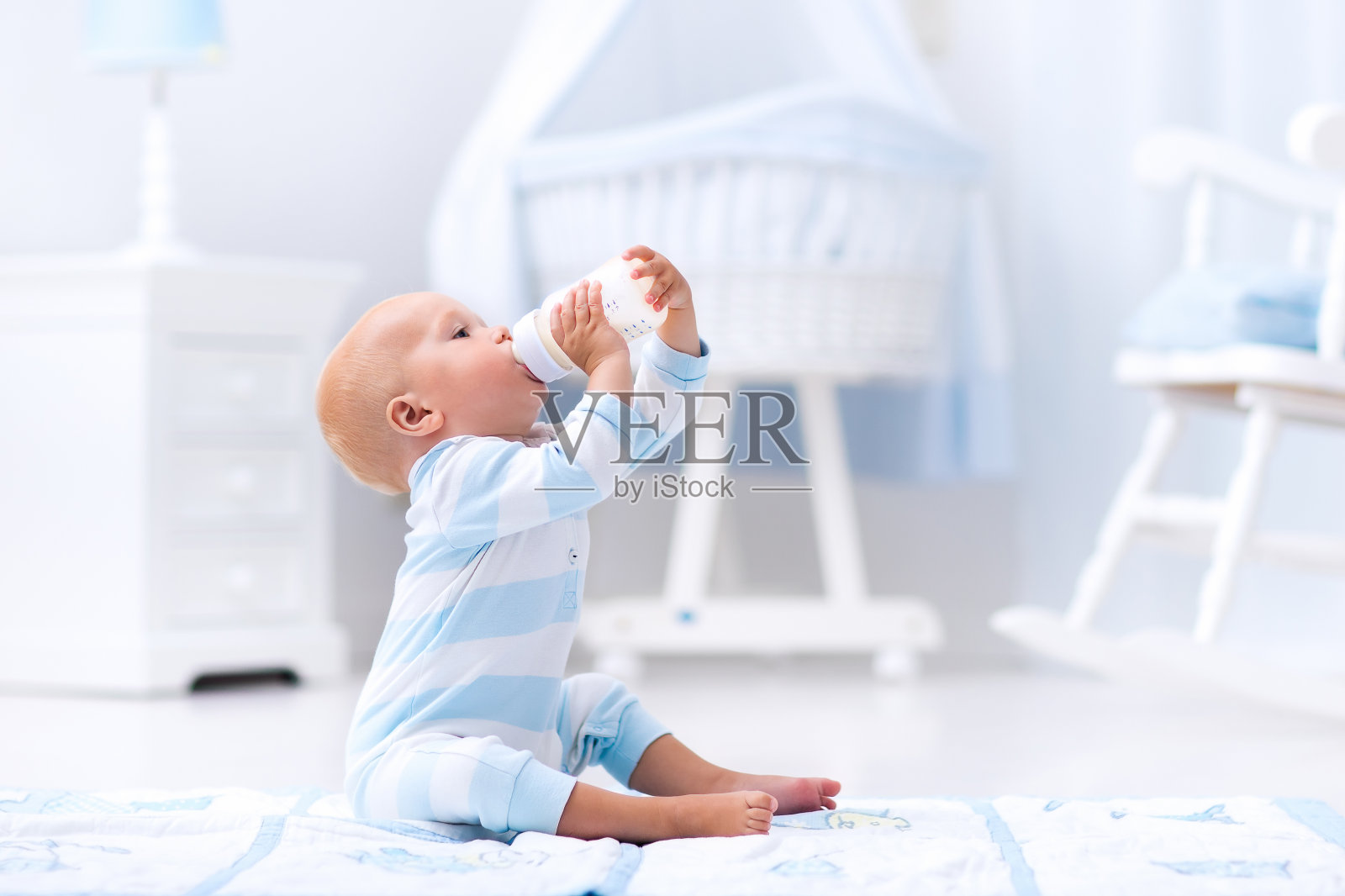 在阳光明媚的育婴室里，男婴正在喝奶瓶里的牛奶照片摄影图片