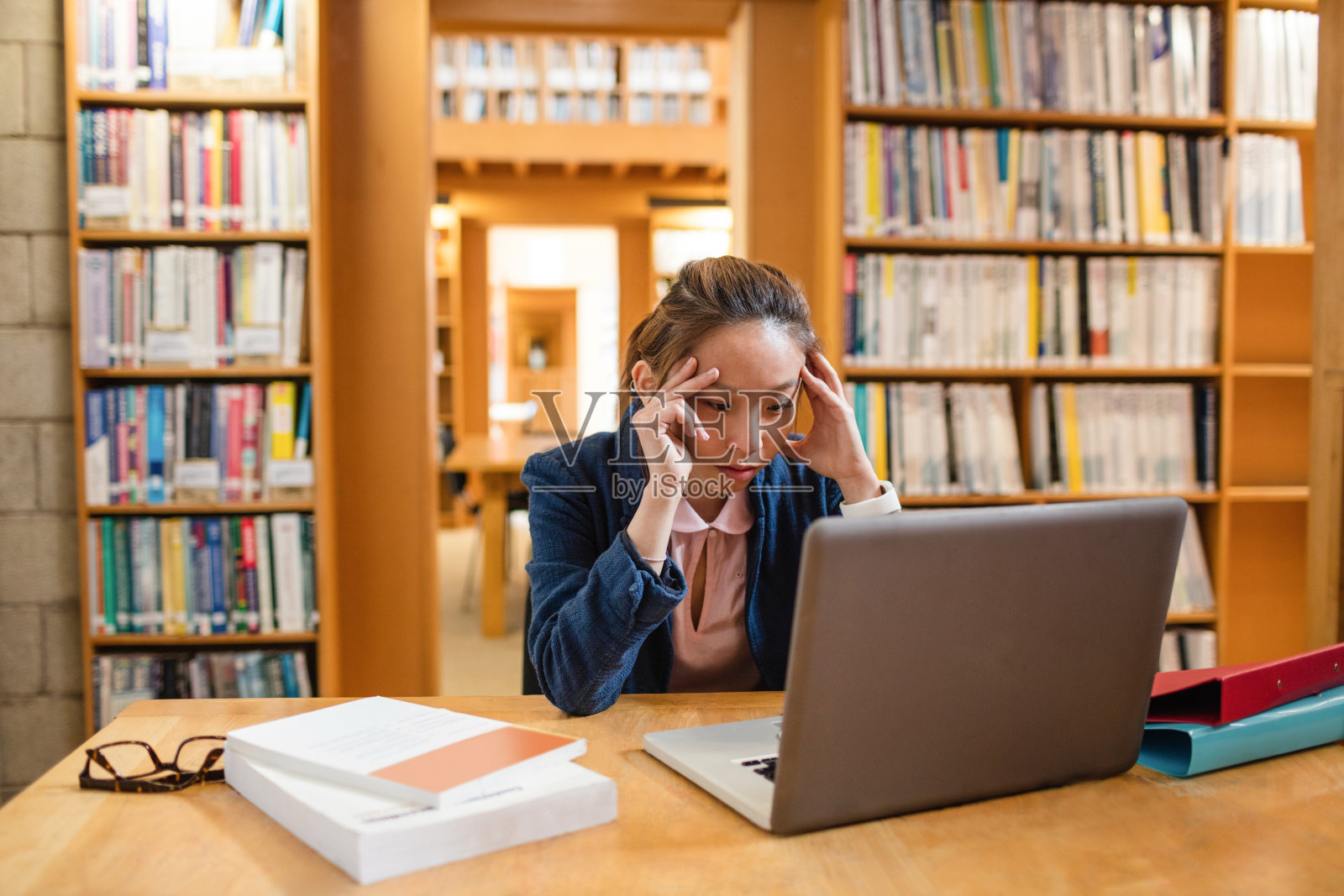 紧张的年轻女子在图书馆使用笔记本电脑照片摄影图片