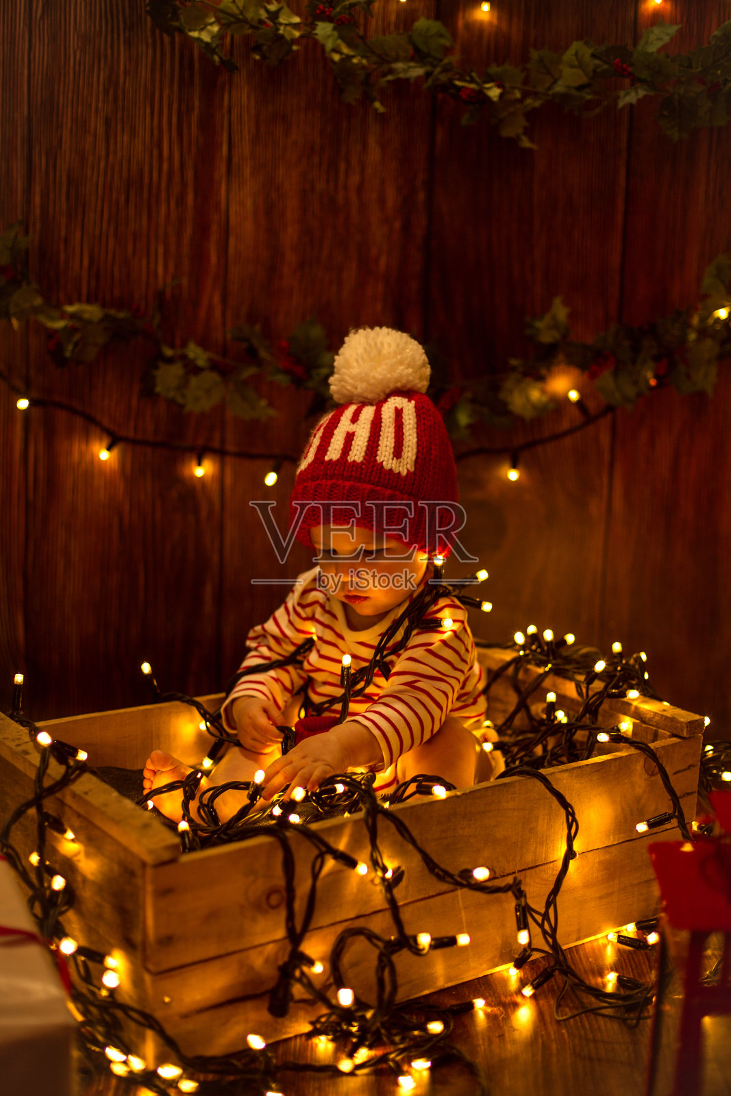 可爱的孩子坐在盒子里，包裹在圣诞彩灯里照片摄影图片