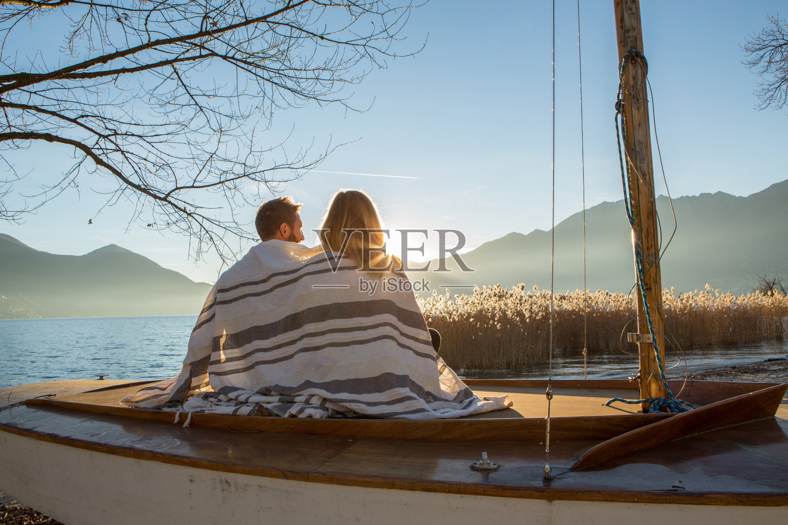 一对年轻夫妇裹着毯子在湖边看日落照片摄影图片