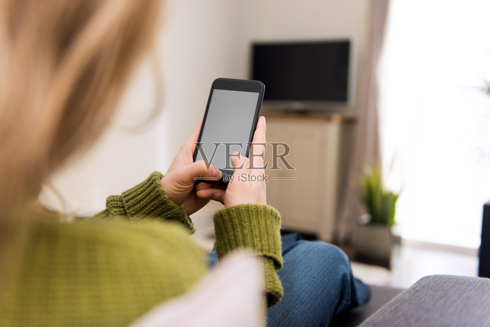 金发女人正坐在家里看着手机屏幕上的技术背景照片摄影图片