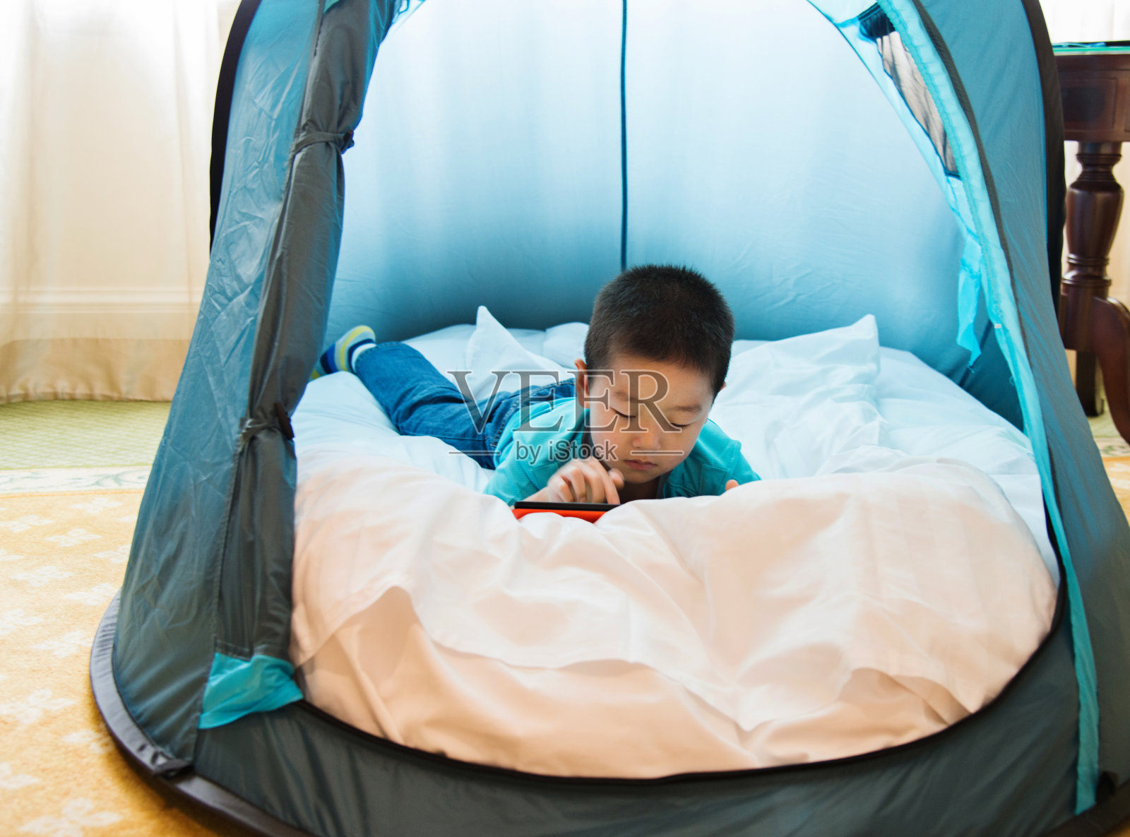 一个亚洲小男孩在帐篷里玩平板电脑照片摄影图片