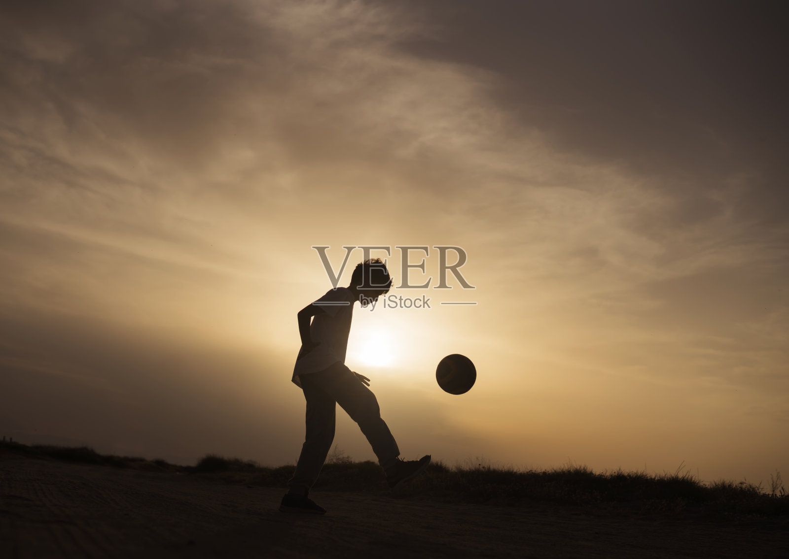 男孩在日落时踢足球照片摄影图片
