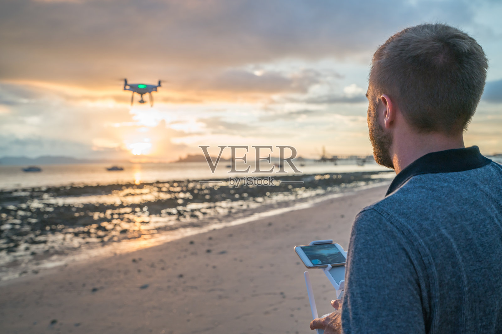 日落时分，一名年轻人在热带海滩上驾驶无人机照片摄影图片