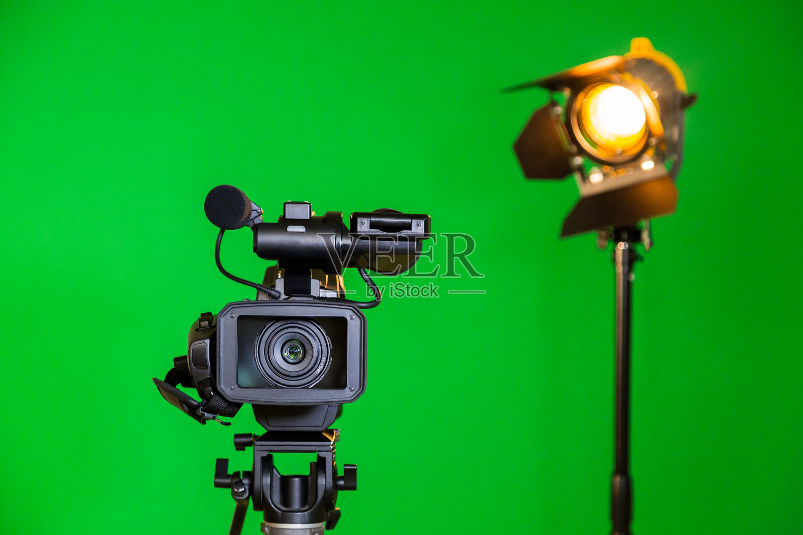 一个摄像机和一个聚光灯，一个菲涅耳透镜在绿色背景上。在室内拍摄。色度键照片摄影图片