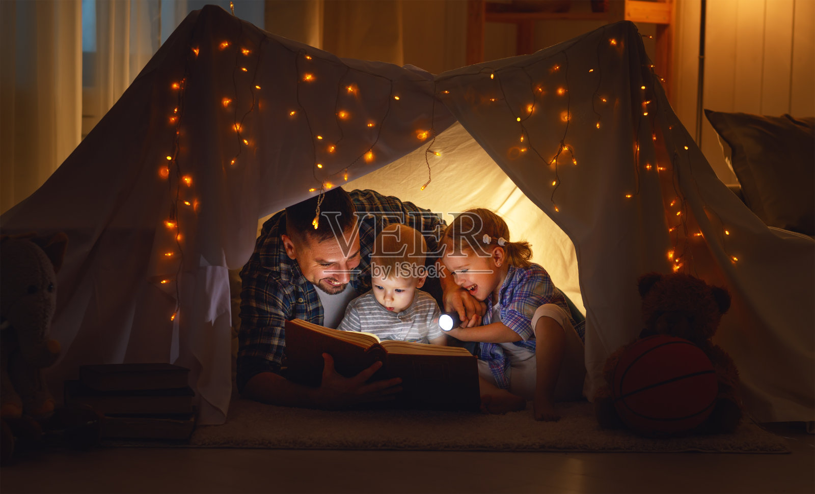 快乐的家庭，爸爸和孩子们在家里的帐篷里看书照片摄影图片