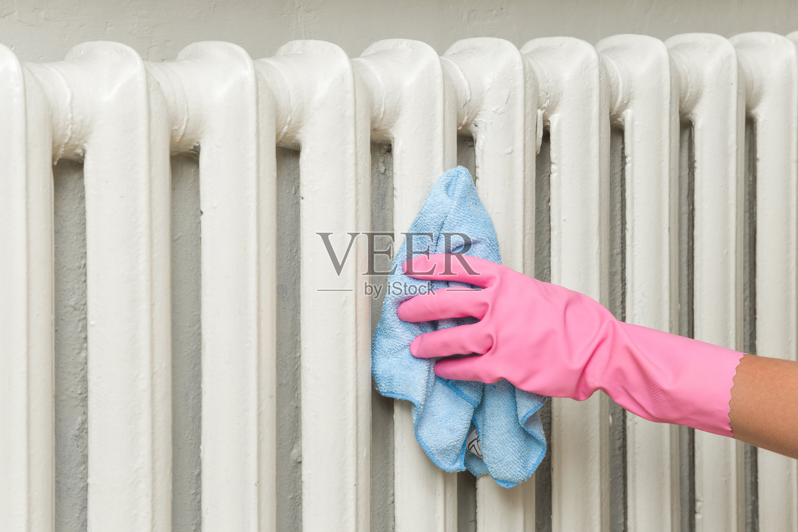 把粉红色的橡胶防护手套和抹布放在一起擦拭加热器散热器。早春大扫除或定期大扫除。女保洁员打扫房子。照片摄影图片