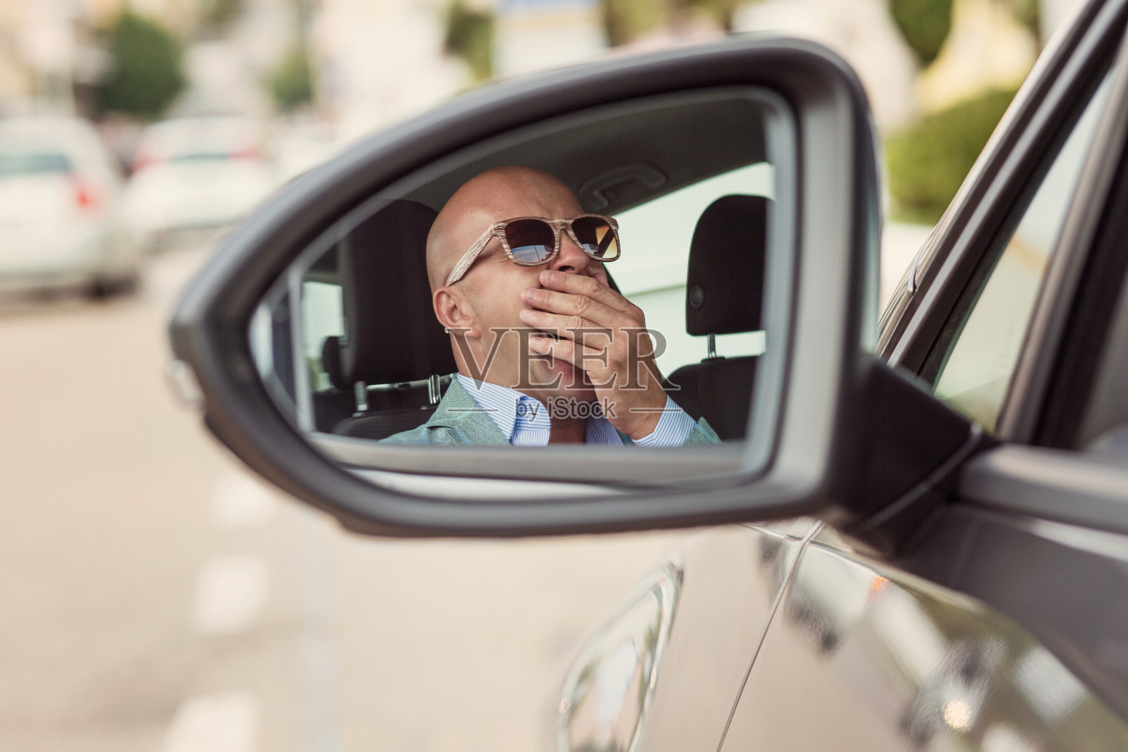 侧镜的视图反射，困倦疲倦，疲劳，打呵欠，疲惫的年轻人戴着太阳镜，驾驶他的汽车在交通经过长时间的驾驶。交通睡眠剥夺事故概念照片摄影图片