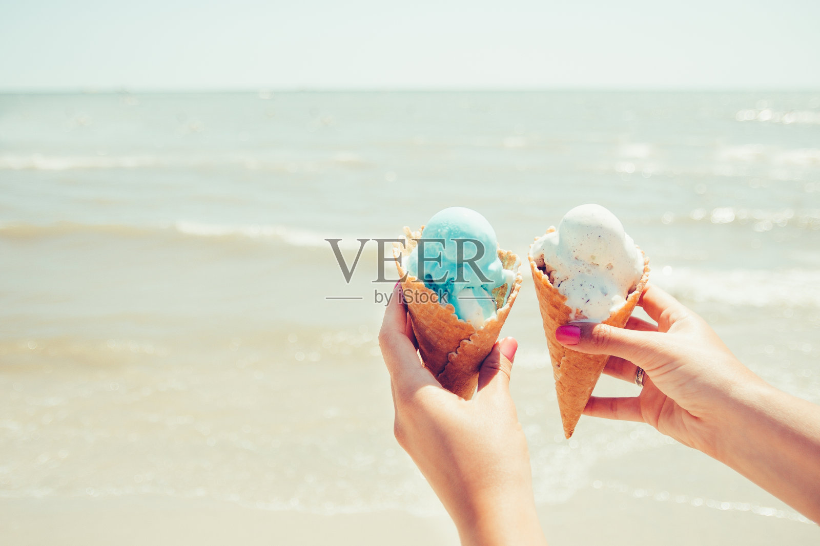女人的手拿着两个冰淇淋在海上的背景。夏天。假期。照片摄影图片
