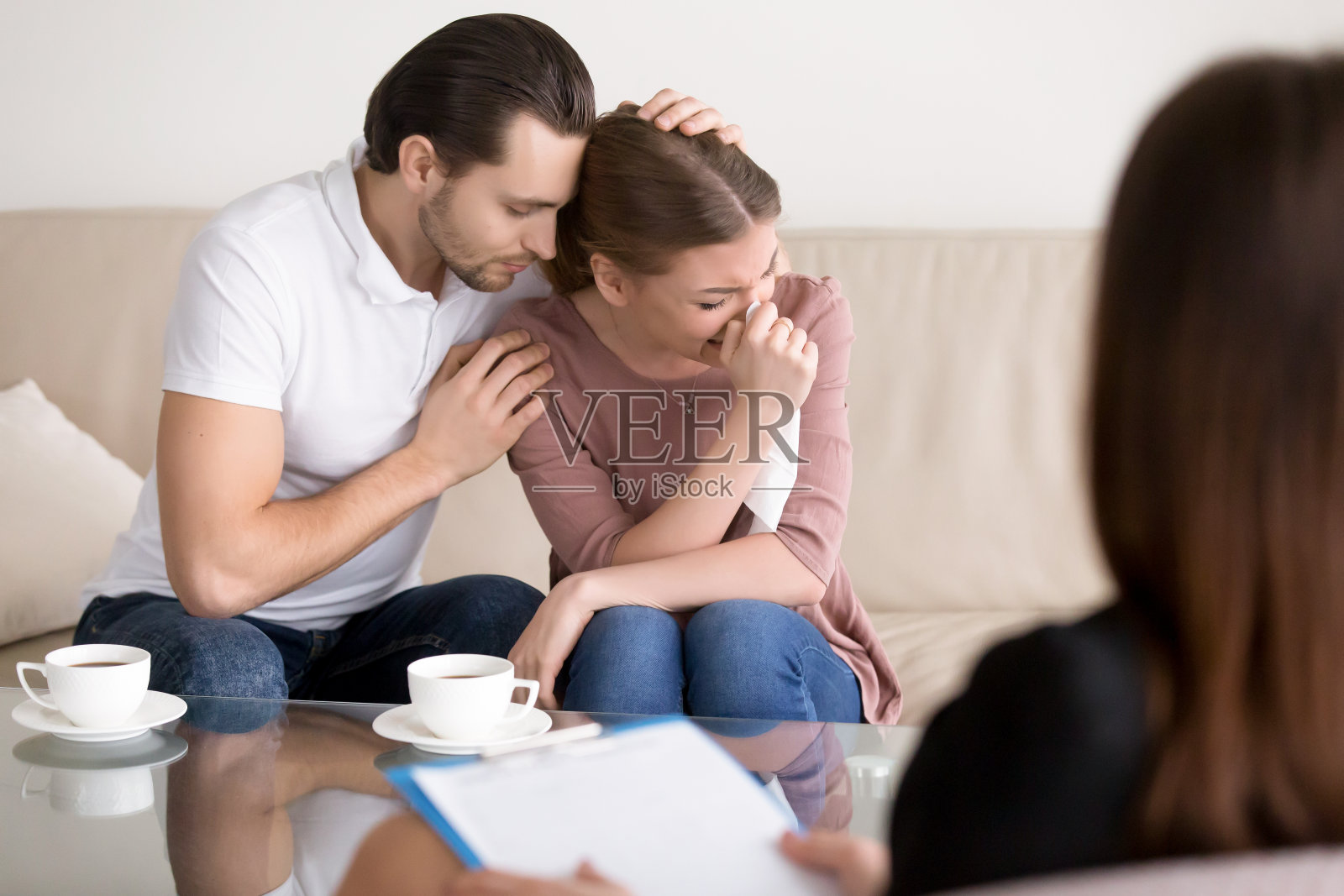 家庭辅导。丈夫在心理医生那里安慰伤心哭泣的妻子照片摄影图片