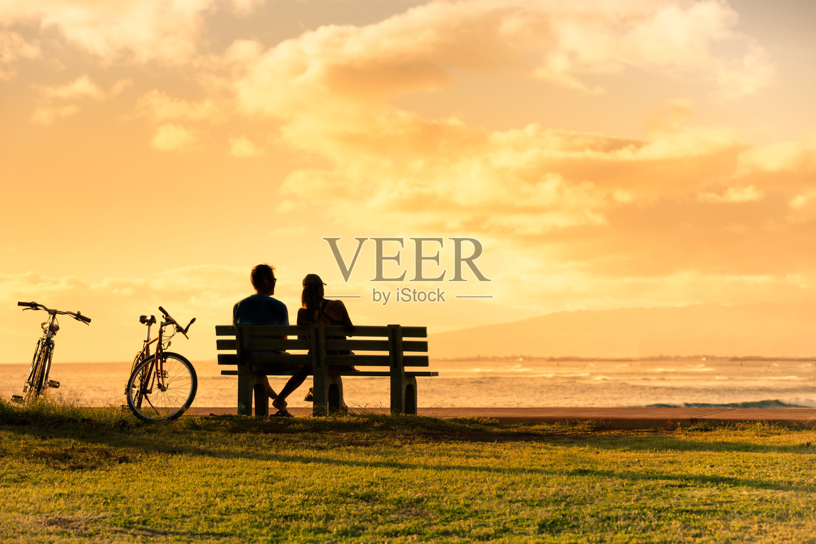 一对夫妇坐在公园长椅上看日落。照片摄影图片