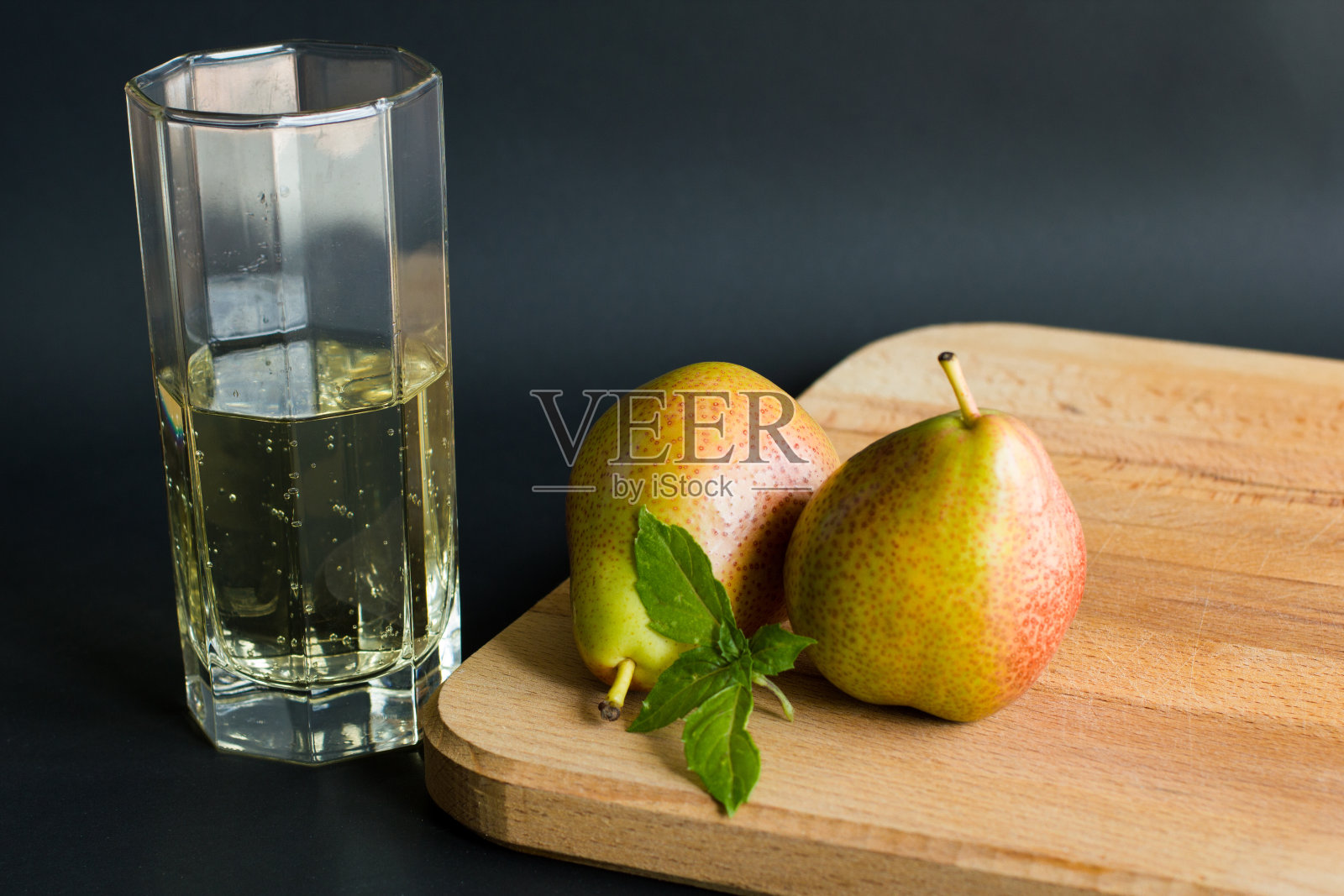 软的不含酒精的梨苹果酒在一个透明的玻璃和两个新鲜的罗勒叶的梨切板上有黑色的背景照片摄影图片
