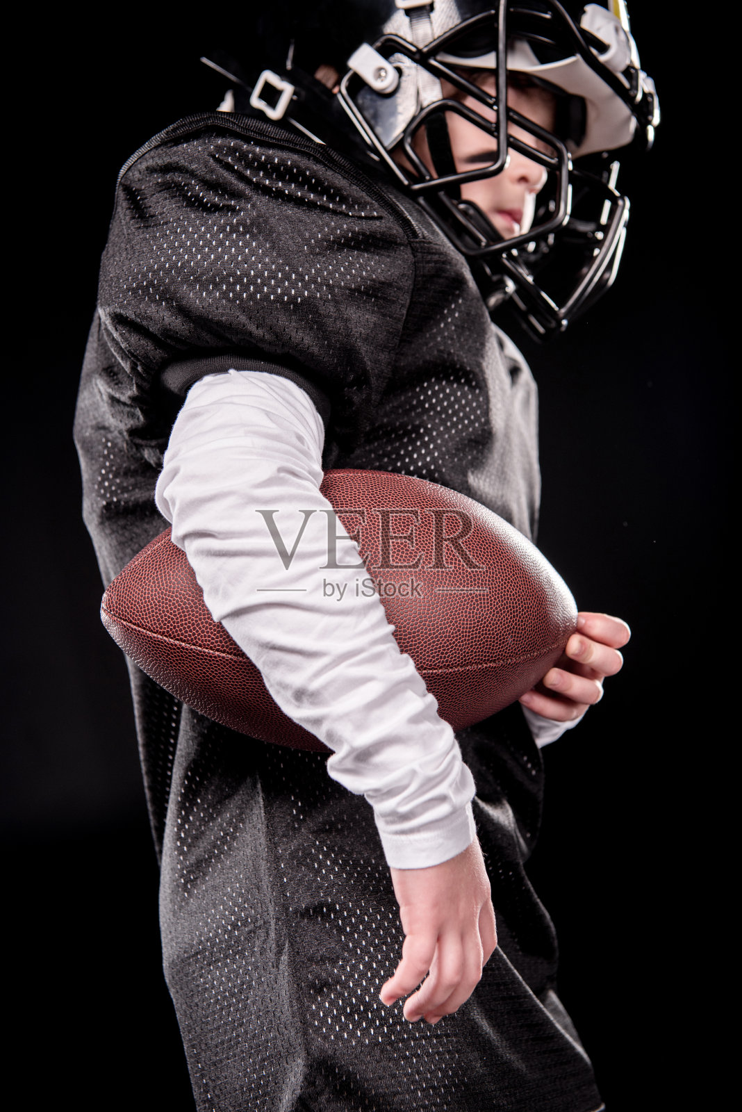 低角度的男孩美国足球运动员抱着橄榄球在黑色照片摄影图片