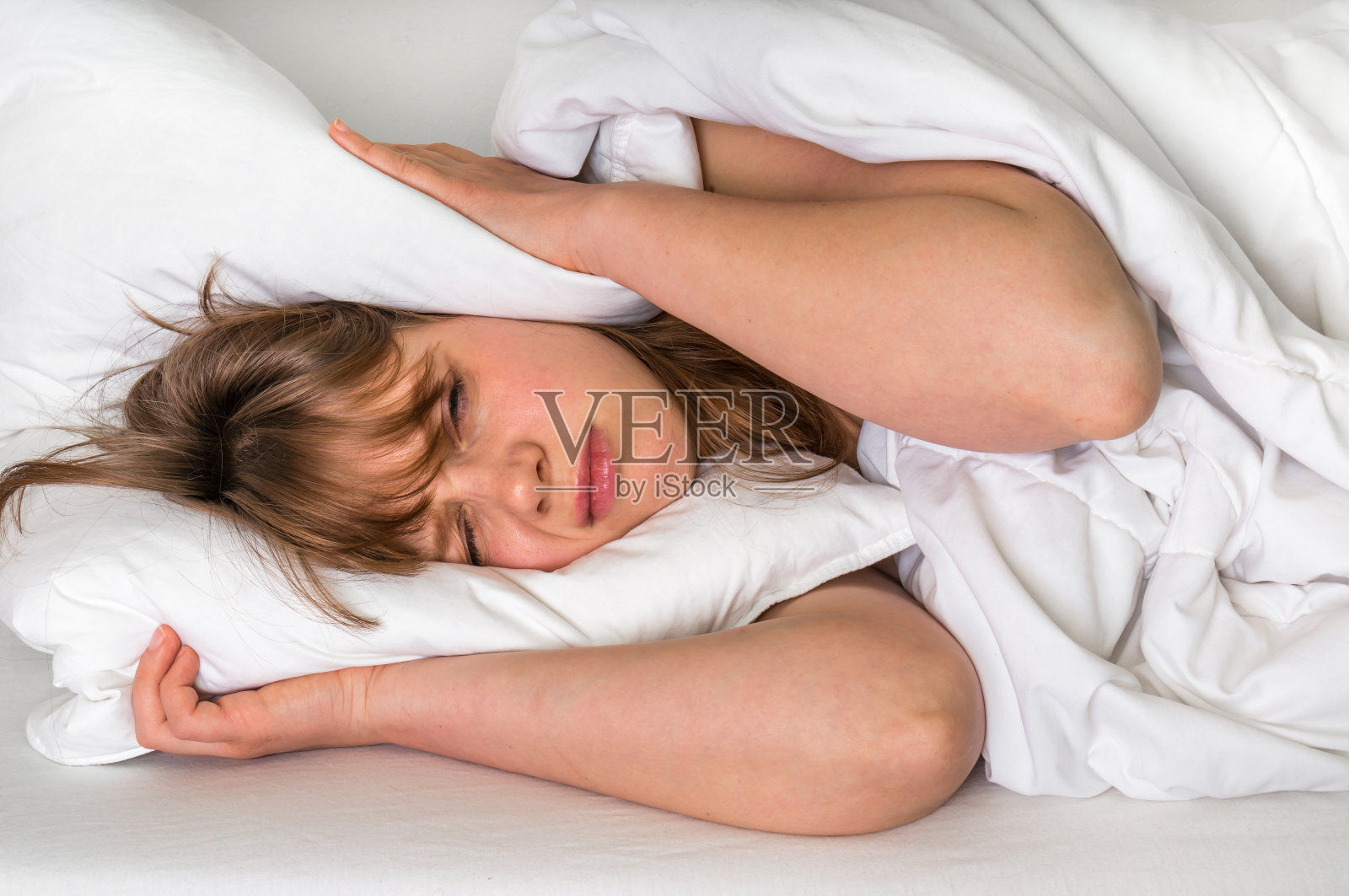 女人想睡觉，她用枕头捂住耳朵照片摄影图片