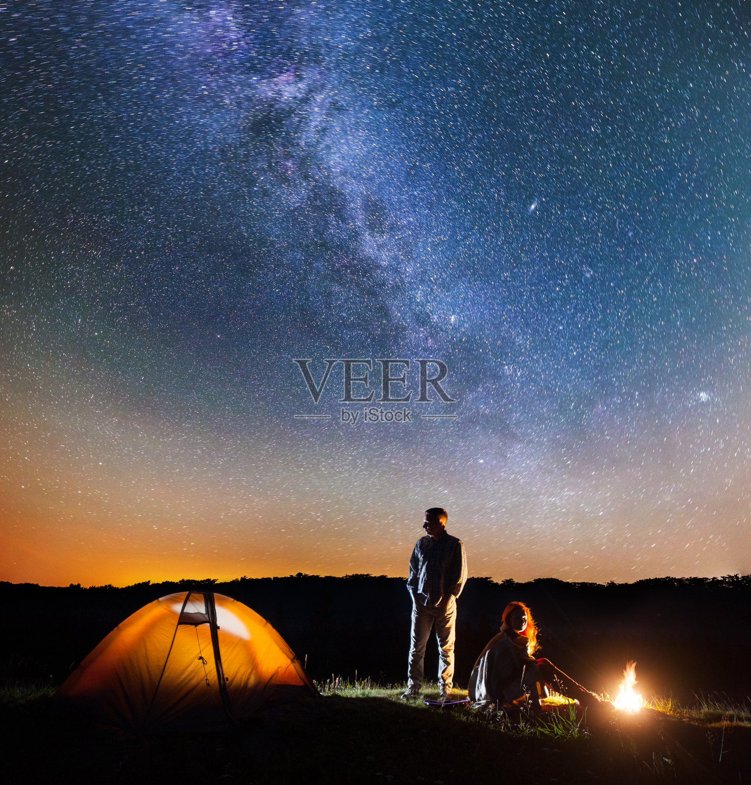 一对浪漫的徒步旅行者在他的营地在晚上靠近篝火和帐篷对星空与银河照片摄影图片